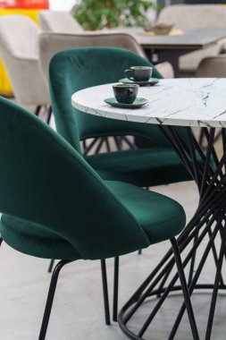 Beyaz ahşap masa, yumuşak kumaş döşemeli yeşil ahşap sandalyelerle tamamlanmış. Yeşil fincanlar ve tabaklar masanın üstünde.