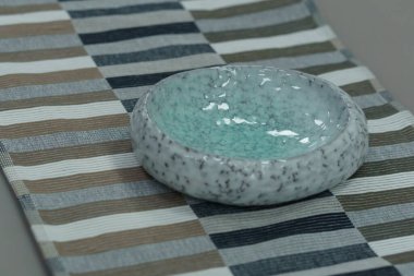 Bej ahşap masa, bej koltuklar ve yumuşak kumaş döşeme. Masada yeşil çay tabağı var.