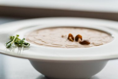 Mantarlı krema çorbası ve beyaz tabakta otlar.