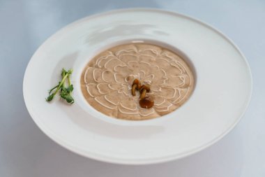 Mantarlı krema çorbası ve beyaz tabakta otlar.