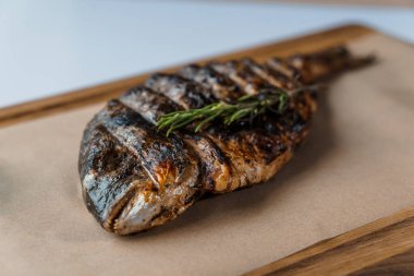 Ahşap bir tahtanın üstünde ızgarada limon ve biberiyeyle pişirilmiş Dorado balığı