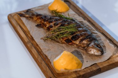 Ahşap bir tahtanın üstünde ızgarada limon ve biberiyeyle pişirilmiş Dorado balığı