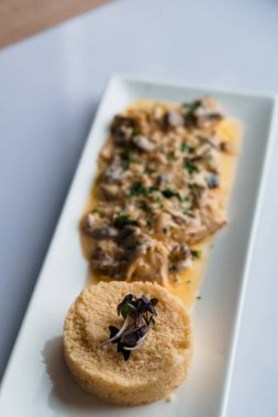 Beyaz seramik tabakta et ve mantar soslu kuskus lapası.