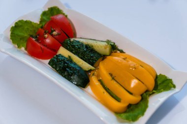 Taze sebzeler, sarı biber ve salatalık masada beyaz bir tabakta.