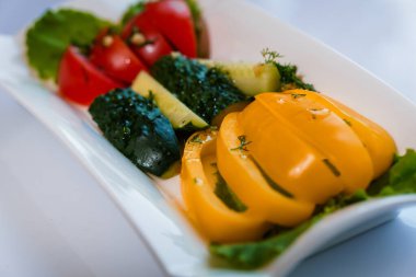 Taze sebzeler, sarı biber ve salatalık masada beyaz bir tabakta.