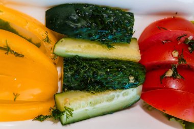 Taze sebzeler, sarı biber ve salatalık masada beyaz bir tabakta.