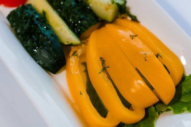 Taze sebzeler, sarı biber ve salatalık masada beyaz bir tabakta.