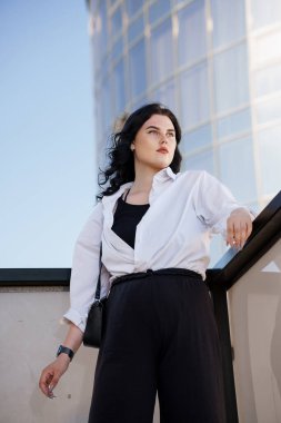 Siyah pantolonlu ve beyaz gömlekli bir iş kadını. Bir iş merkezinin geçmişine karşı siyah takım elbiseli bir iş kadını.