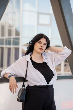 Siyah pantolonlu ve beyaz gömlekli bir kız. İş kadını, siyah takım elbiseli, siyah deri çantalı, bir iş merkezinin arka planında.