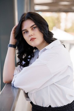 Siyah pantolonlu ve beyaz gömlekli bir kız. İş kadını, siyah takım elbiseli, siyah deri çantalı, bir iş merkezinin arka planında.