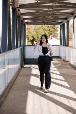 Güneşli bir günde modern şehir köprüsünde yürüyen kendinden emin bir kadın..