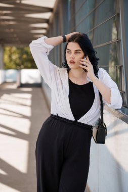 Modern ofis koridorunda kendine güvenen bir iş kadını telefonda konuşuyor..