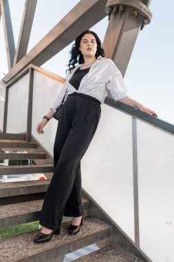 Kendine Güvenen Zarafet: Modern Mimarlık Merdiveninde Moda Kadın Pozu.