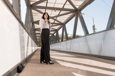 Professional Woman Standing Confidently on Modern Urban Bridge Walkway. clipart