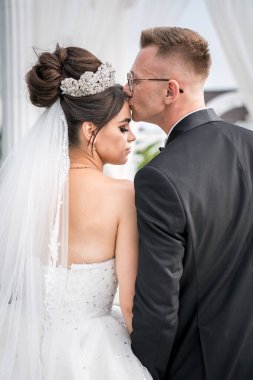 Şık Düğün Anı: Damat Şefkatle Öpüşen Gelinin Alnında Romantik Açık Hava Ayarları.