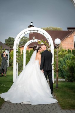 Romantik Düğün Zamanı: Gelin ve Damat Zarif Beyaz Bahçe Archway Altında Yumuşak Bir Öpücük Paylaşıyorlar.