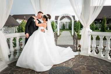 Büyüleyici düğün öpücüğü Narin bir beyaz çardakta yemyeşil ortamda.