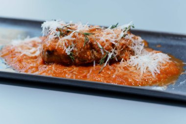 Zengin domates soslu gurme köfte Taze otlar ve siyah tabakta peynirle süslenmiş.