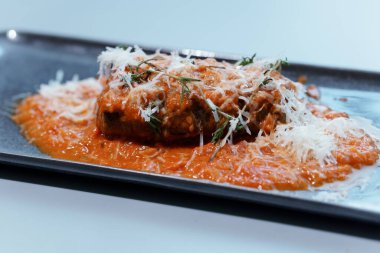 Zengin Domates Sosu ve Zarif Koyu Tabakta Taze Parçalanmış Peynir ile Parmesanlı Gurme Patlıcan.