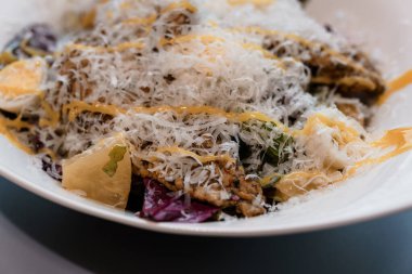 Izgara tavuklu taze Sezar salatası ve zarif beyaz tabakta tıraş edilmiş parmesan peyniri.