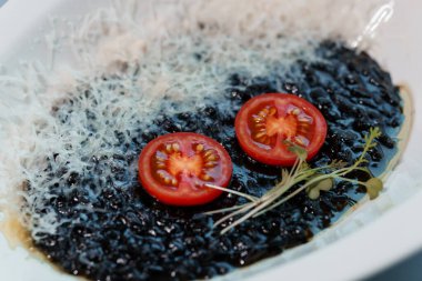 Dilimlenmiş domates dilimleri ve parmesanlı mikro yeşilliklerle garnitürlü Black Rice Risotto..