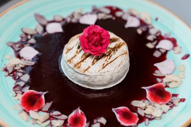 Bir Cheesecake Tatlısında Gurme Sanatçılık Zengin Sosu, Yenilebilir Çiçekler ve Seramik Tabakta Badem Dilimleri.