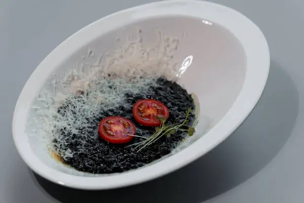 stock image Elegant Gourmet Black Risotto with Cherry Tomatoes and Parmesan Garnish in Modern White Bowl.