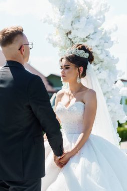 Beyaz Gelinlikli Gelinle Zarif Açık Düğün Töreni ve Çiçekli Archway 'in Ortasında Siyah Takım Elbiseli Damat.
