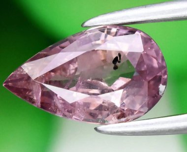 Exquisite Pear-Shaped Pink Diamond Held in Tweezers Against Green Background. clipart