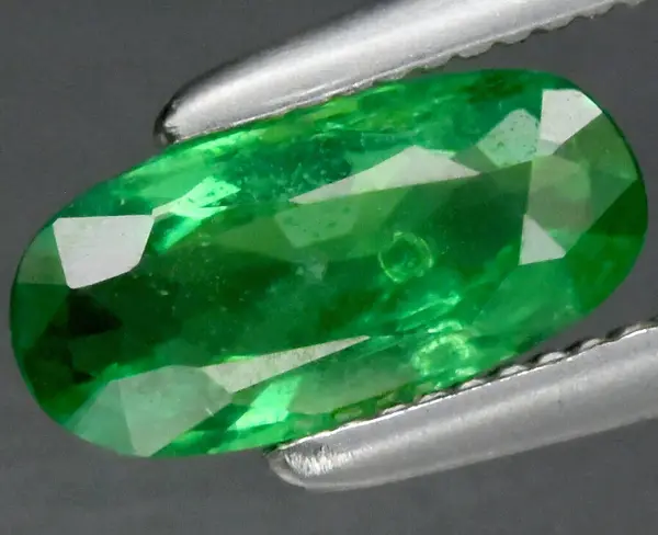 stock image Close-up of Brilliant Green Emerald Gemstone in Precision Tweezers Displaying Faceted Cut and Vivid Color.