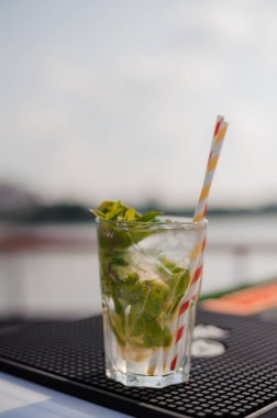 Refreshing Mojito Cocktail with Fresh Mint Leaves and Striped Straw on a Sunny Day by the Water. clipart