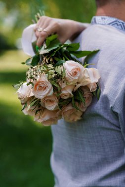 Zarif pembe gül buketi, yemyeşil yeşilliklerle çevrili şık bir ortamda bir insanın elinde..