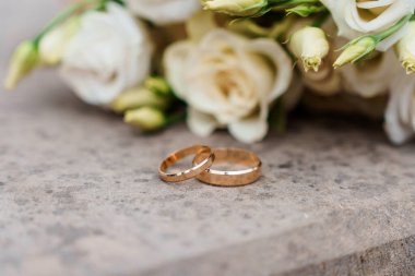 Zarif alyanslar, arka planda bir buket krem gülle dokulu bir yüzeyde dinleniyor..