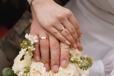 Sarmaş dolaş Ellerin Romantik Yakın Çekimi Evlilik Yüzükleri ve Krem Güller Buketi Sevgi ve Bağlılığı simgeliyor.
