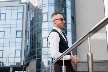 Modern bir cam binanın önünde kendinden emin bir şekilde duran şık bir işadamı..