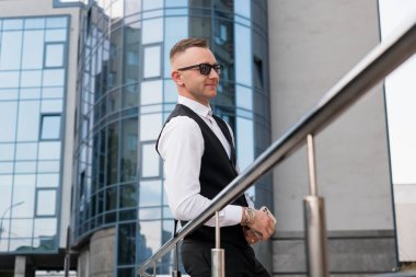 Modern Cam Binası 'nın yakınında güneş gözlüklü şık genç adam pozu.