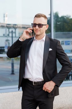 Şık takım elbiseli şık bir adam dışarıda telefonla konuşuyor..