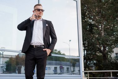 Akıllı giyimli sofistike bir iş adamı açık havada telefon görüşmesi yapıyor..