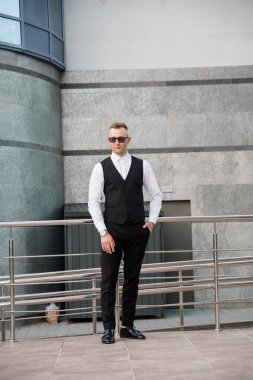 Açık havada güneş gözlüğü pozu veren resmi kıyafetli zarif adam..