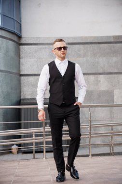 Şık giyinmiş, güneş gözlüklü, açık havada poz veren zarif adam..