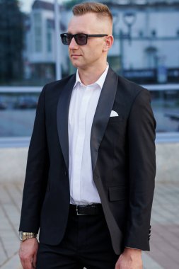 Siyah takım elbiseli, güneş gözlüklü, açık havada poz veren zarif adam..