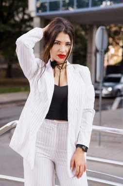 Beyaz çizgili takım elbiseli şık genç bir kadın, güvenli bir şekilde dışarıda poz veriyor..