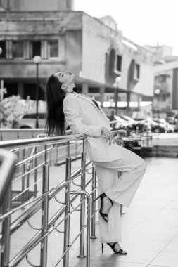 İnce çizgili takım elbiseli şık bir iş kadını şehir planına karşı kendine güvenen bir poz veriyor..