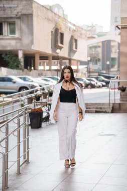 Kentin Mimarisi Ortasında Çizgili Kıyafetlerle Gezen Kendinden emin Genç Kadın.