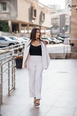 İnce çizgili takım elbiseli zarif iş kadını şehir ortamında güvenle yürüyor..