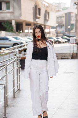 Şık bir iş elbisesi içinde modern bir şehir ortamında rahatça yürüyen şık genç bir kadın..
