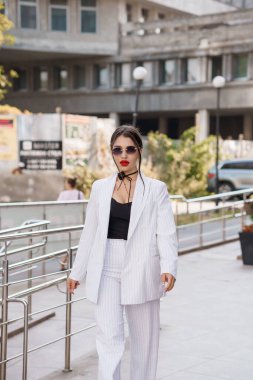 Şık çizgili takım elbiseli şık bir kadın şehir ortamında rahatça yürüyor..