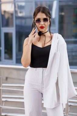 Stylish Woman in Pinstripe Suit With Sunglasses and Bold Red Lips Posing Confidently Outdoors. clipart