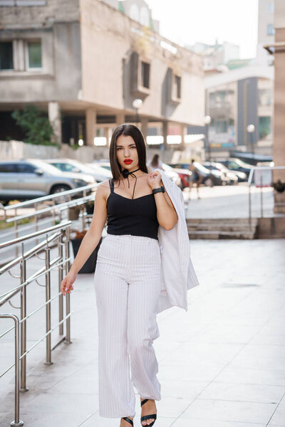 Стильная молодая женщина уверенно прогуливается по городским окрестностям в модном наряде.