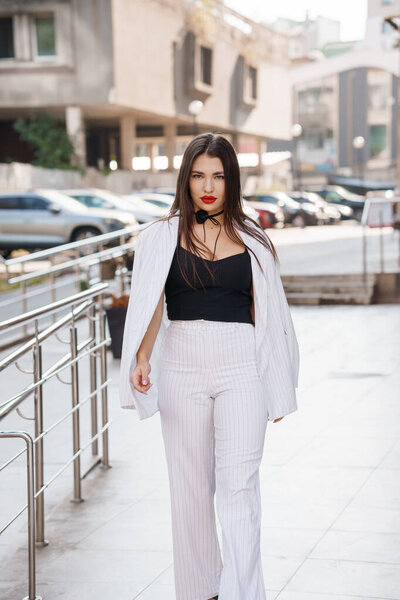 Модная молодая женщина в стильном костюме в полоску уверенно прогуливаясь по городской среде.